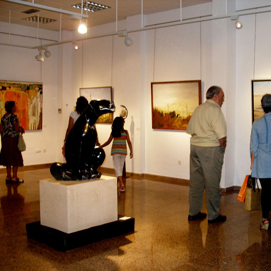 Photo of a paintings exhibition that had paintings of Andreina Scanu. You can see people looking at the paintings inside the museum.